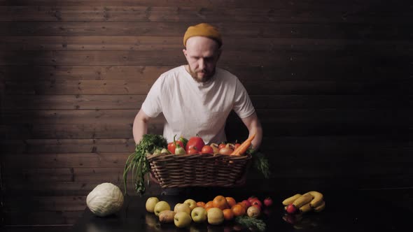 a Happy Farmer in a White Tshirt and Hat Holds a Basket of Fresh Fruits and Vegetables