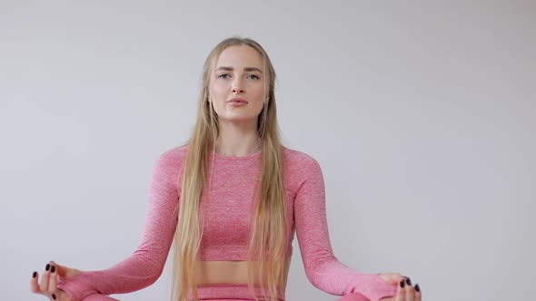 Pretty girl is sitting on the floor in lotus position with hands-on knees and meditating