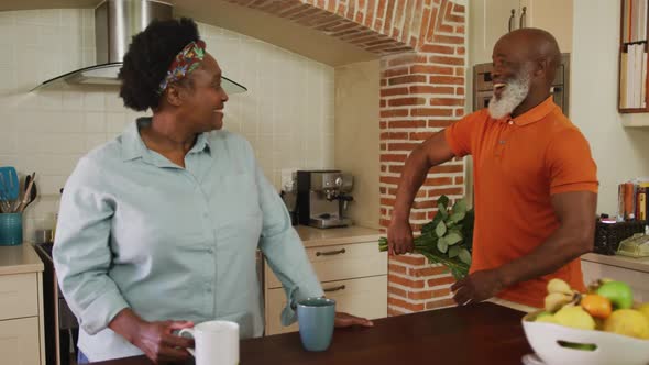 African american senior man giving a bouquet of flowers to senior woman in the kitchen at home