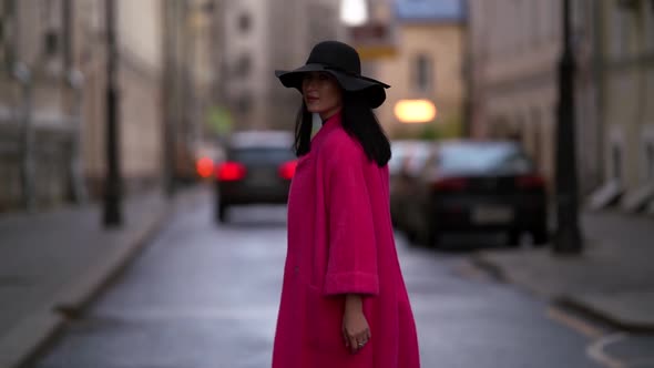 A Woman a Black Hat and a Purple Coat Walks Confidently on the Street in a Crowded City. It Is