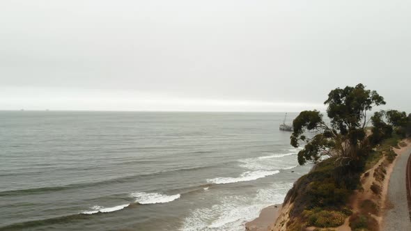 AERIAL Drone shot above California Bluffs and stormy ocean with train tracks.