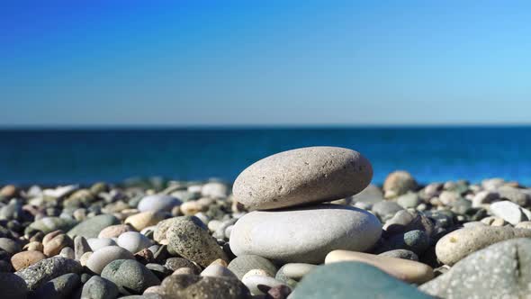 A woman's hand makes a pyramid of stones on the background of the sea or ocean.