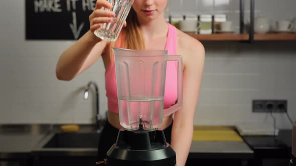 A female athlete makes a protein shake (pouring water and pouring protein powder into a blender)