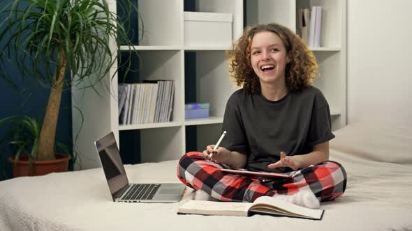 Cute Teenage Girl Doing Homework While Sitting on the Bed at Home