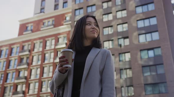 Low Angle Portrait of an Asian Businesswoman on a Modern City Street with Coffee