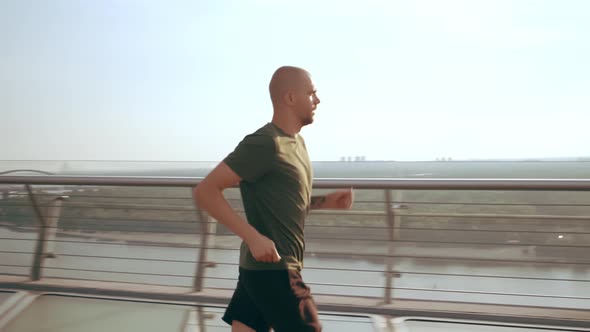 Young Man in Sports Uniform Runs on the Pedestrian Bridge at Dawn
