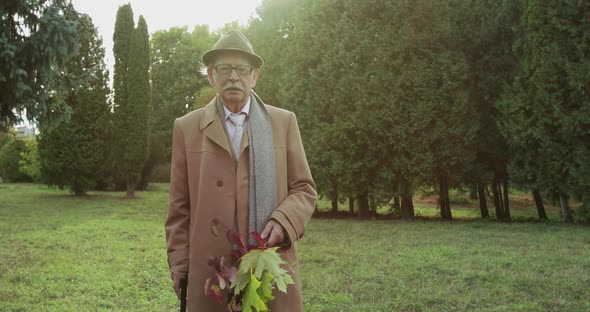 Portrait of Sad Lonely Senior Man Stands Among Park Lawn and Looks at Camera