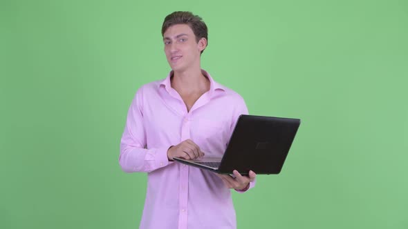 Happy Young Handsome Businessman Talking While Using Laptop