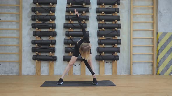 Young Athletic European Woman Doing A Stretching Exercise in the Gym, Dressed in Black Sportswear