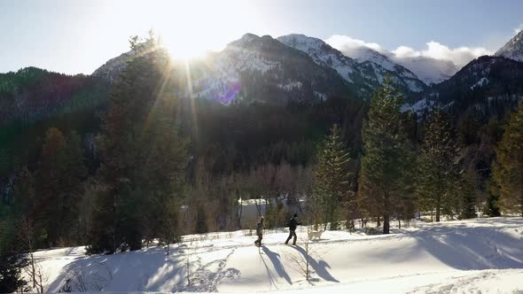 Couple snowshoeing uphill with their dog as sun peaks over mountain top