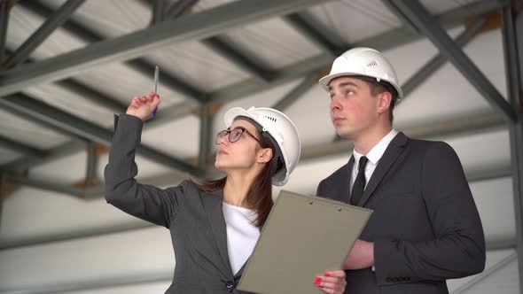 The Man Approves the Project. Young Man and Woman in Helmets with Documents at a Construction Site