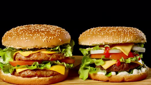 Close-up of Two Appetizing Burgers with Sesame Buns Rotating on Black Background, of Fast Food