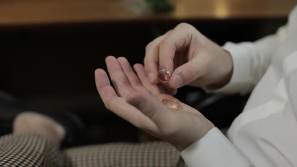 Groom in a White Shirt Holding Wedding Rings on the Palm of His Hand. Man Touches the Rings