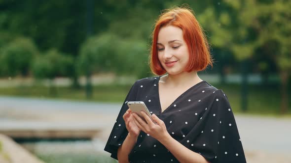 Pretty Caucasian Lady Girl Stand Outdoors in City Park Look at Mobile Phone Use Urban Wifi Beautiful