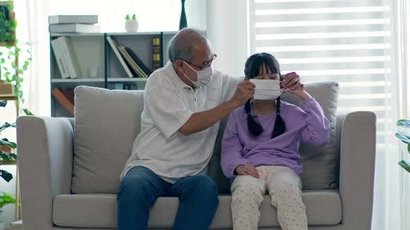 Asian Elderly grandfather hug grandchild and wearing face mask on sofa