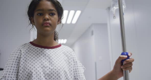 Mixed race girl walking with drip bag in hospital room