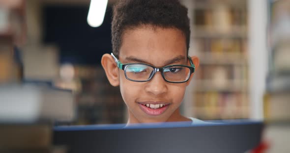 Close Up of Preteen African Boy Student Smiling Typing on Laptop Working at School Library