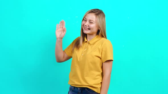 The Happy Young Woman Says Hello Raising a Hand Up and Smiles.