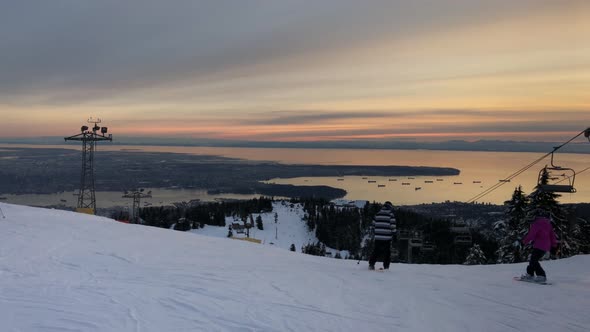 People skiing downhill on Cypress mountain at dusk, Vancouver in background