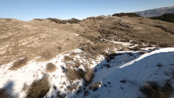 Flying over trees and bushes in a snow covered mountains landscape with an FPV drone