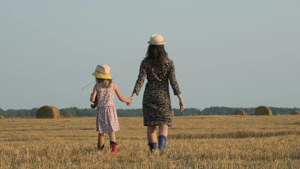 Woman with Daughter Walk in Field with Haystacks