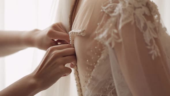 Bridesmaid Ties and Helps Put on Wedding Dress Morning Preparation of the Bride with White Gown