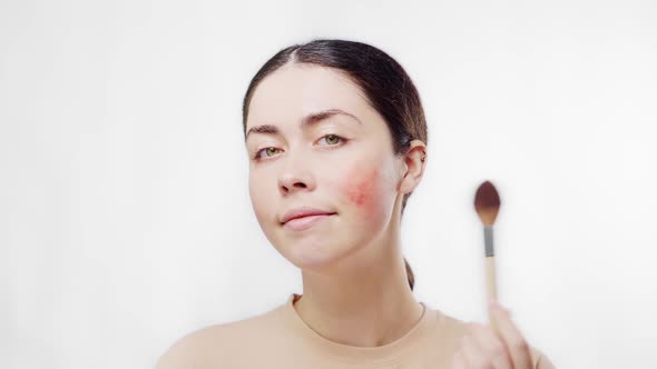 Portrait of a young beautiful woman make ups with brush and powder the redness on her cheek.