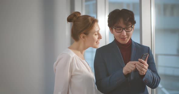 Asian Businessman Showing Report on Smartphone To Caucasian Female Colleague