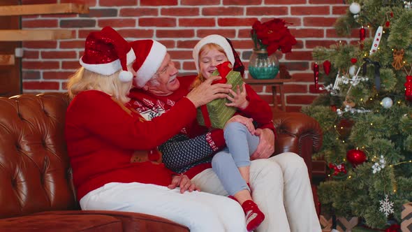 Grandfather Grandmother Gifting Christmas Present Box to Amazed Happy Grandchild Girl Kid at Home