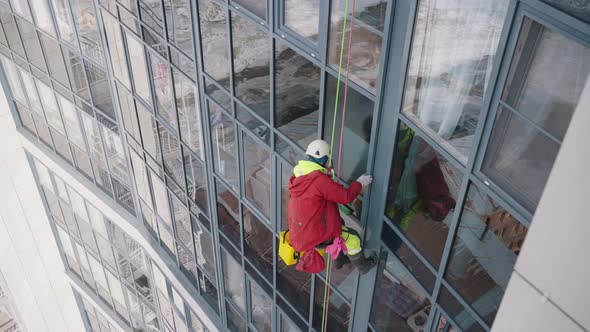 Climber in Overall and Helmet Washes Windows of Skyscraper