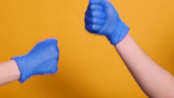 Handshake of Two People in Blue Medical Gloves on a Yellow Background