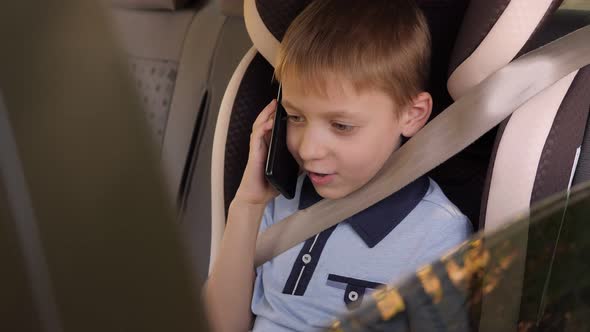 A Little Child is Talking on the Phone While Sitting in a Car Seat in the Summer