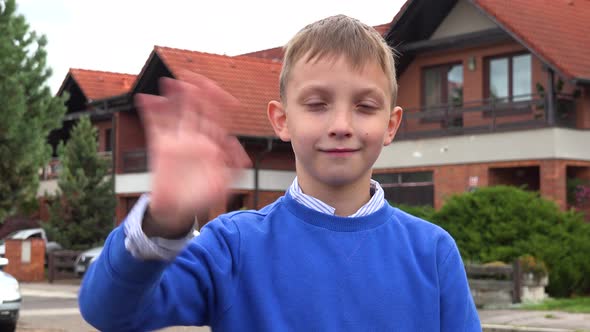 A Young Boy Smiles and Waves at the Camera in a Suburban Street