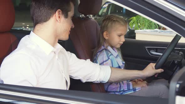 Little Girl Is Sitting at the Steering Wheel of a New Car