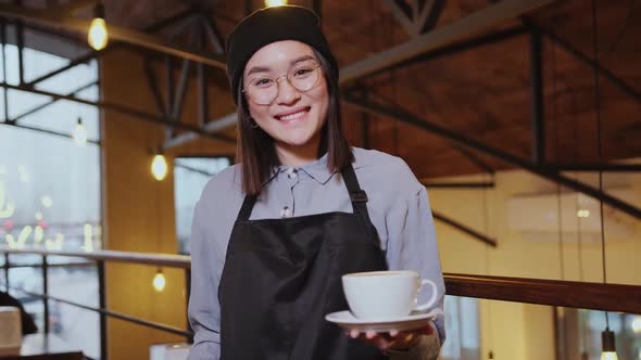 Friendly Asian Female Waitress Holding Coffee Cup and Looking at Camera