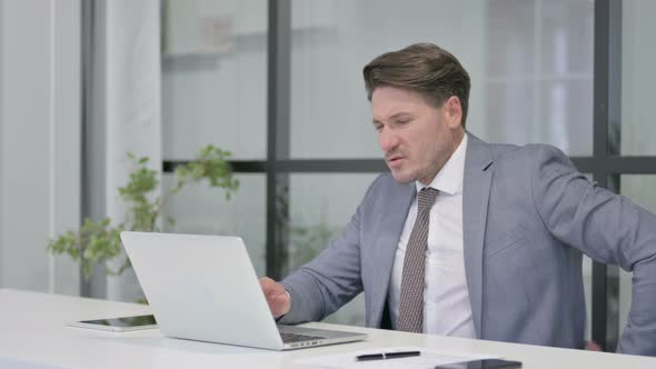 Middle Aged Man having Back Pain while using Laptop in Office