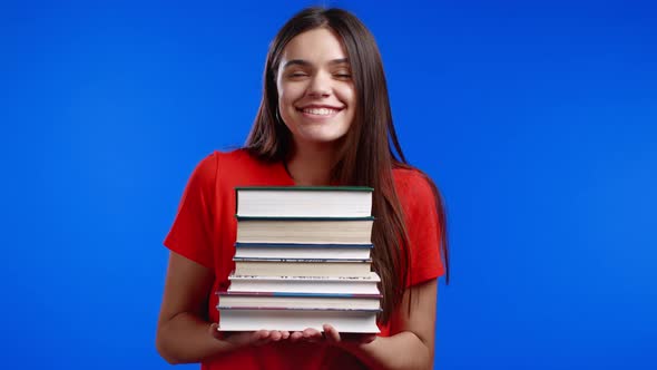 Smiling Woman As Student on Blue Background Holds Stack of University Books From Library