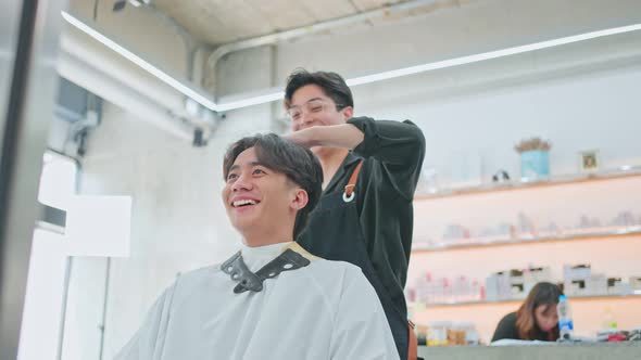 Asian hairdresser barber male use scissors cut hair of attractive man customer in beauty salon shop.