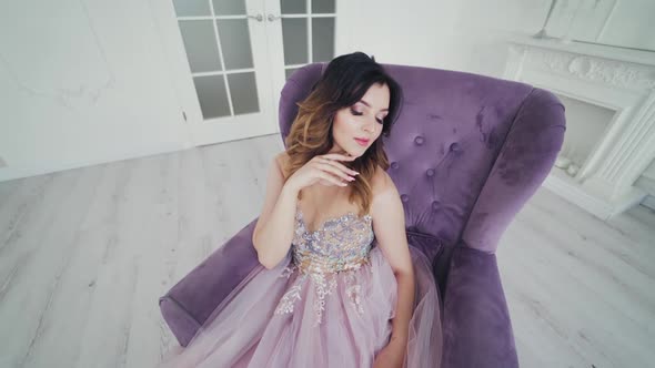Attractive girl in a sexy dress sitting in a purple armchair.