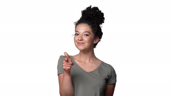 Portrait of Seductive Woman 20s in Casual Tshirt with Hair in Bun Gesturing Finger on Camera Meaning