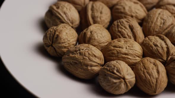 Cinematic, rotating shot of walnuts in their shells on a white surface - WALNUTS