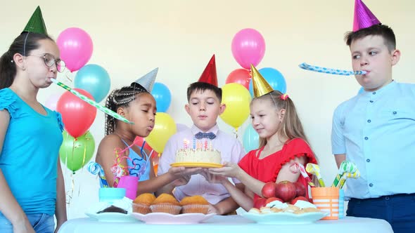 Little Boy Blows Candles While Friends Hold Cake at Birthday