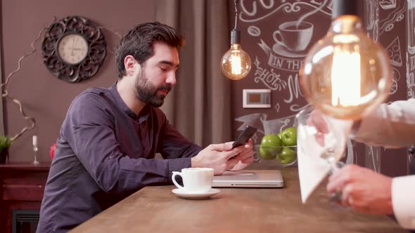 Young Man at a Bar Counter Looks at His Smartphone Screen