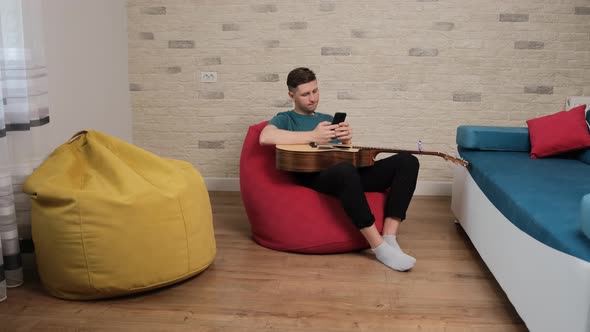 Young Man Sitting with a Guitar in Arms Is Writing an Message To His Girlfriend