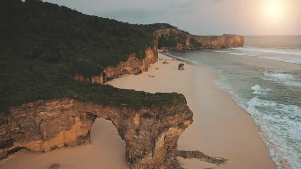 Slow Motion of Ocean Waves Washing Sand Beach at Rock Shore with Green Grass at Top in Aerial View