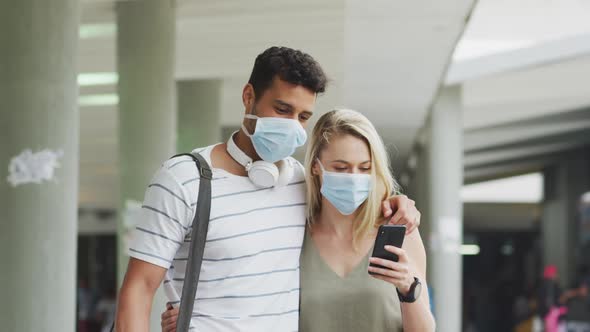 Caucasian couple on the go wearing a coronavirus covid19 mask and using phone