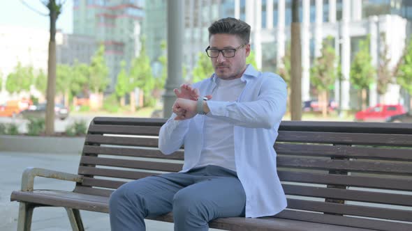 Man Using Smartwatch While Sitting Outdoor on Bench