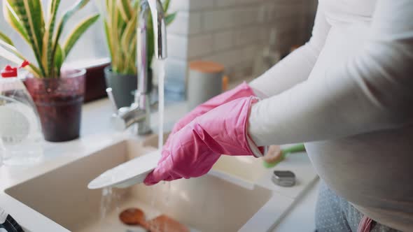 Pregnant woman wearing pink gloves washing dishes