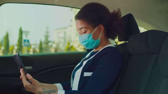 Woman in Protective Mask Using Tablet Pc in Car