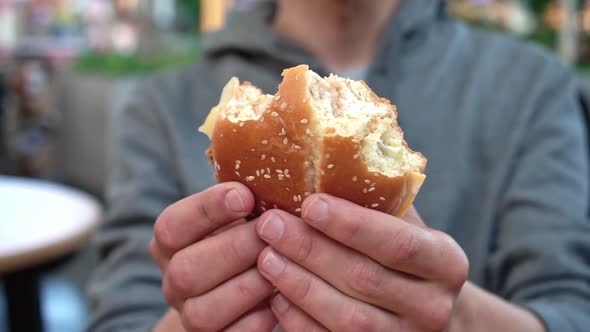 A Man Holds a Bitten Sesame Hamburger on His Outstretched Arms and Slowly Turns It in Front of the